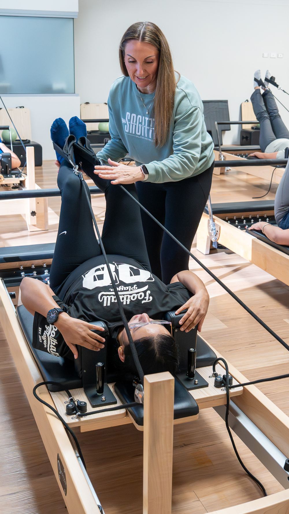 A Sagitta instructor adjusting a member's position on the reformer